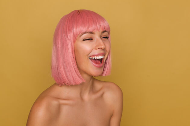 摆姿势可爱的年轻快乐的粉红色头发的女人闭上眼睛 快乐地笑着 站在芥末背景下 赤裸的肩膀随意白色女性