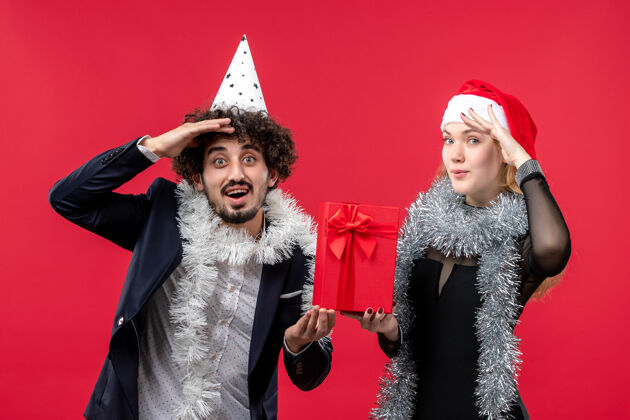 服装正面图：一对年轻夫妇在红墙上拿着新年礼物 表达着圣诞的爱漂亮圣诞节年轻夫妇
