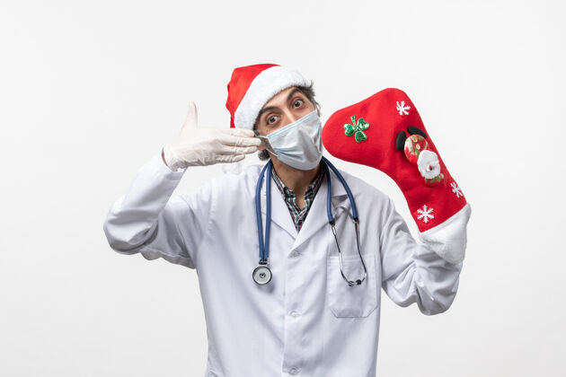 制服正面图白色墙壁上戴着大节日袜子的男医生柯维德圣诞病毒外套视图圣诞节