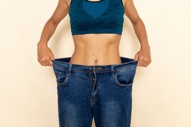 减肥年轻女性的前视图 穿着蓝色衬衫和牛仔裤 身体健康 墙壁为浅白色女运动私人教练