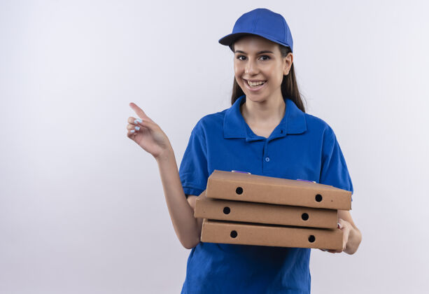 手指身穿蓝色制服 头戴鸭舌帽 拿着披萨盒的年轻送货小姐 手指着侧面 满脸笑容宽指着盒子