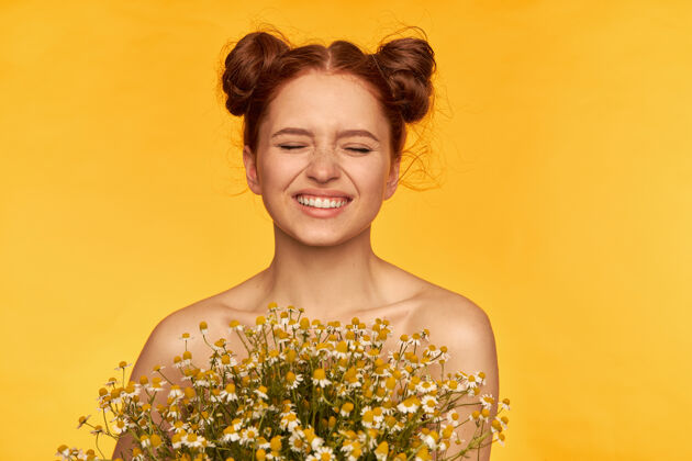 光迷人的 可爱的 迷人的 红头发的小女孩的肖像拿着一束野花 眯着眼睛微笑健康的皮肤特写 孤立地站在黄色的墙上时尚成人长相