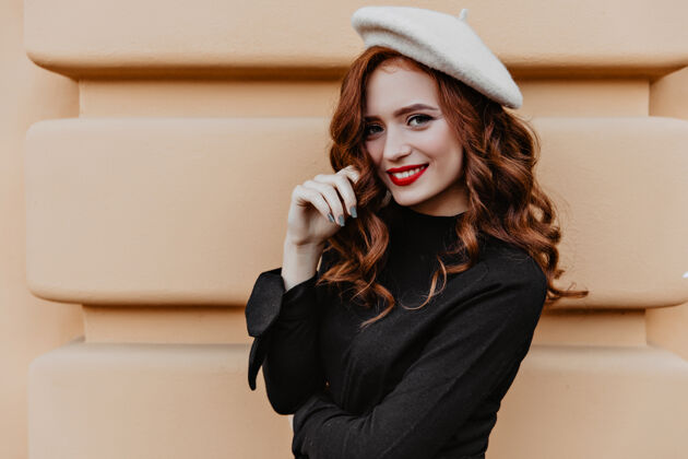 法国一个穿着黑色上衣的高加索女孩在户外摆姿势一个穿着棕色贝雷帽的年轻女子微笑着站在墙边姜配饰秋天