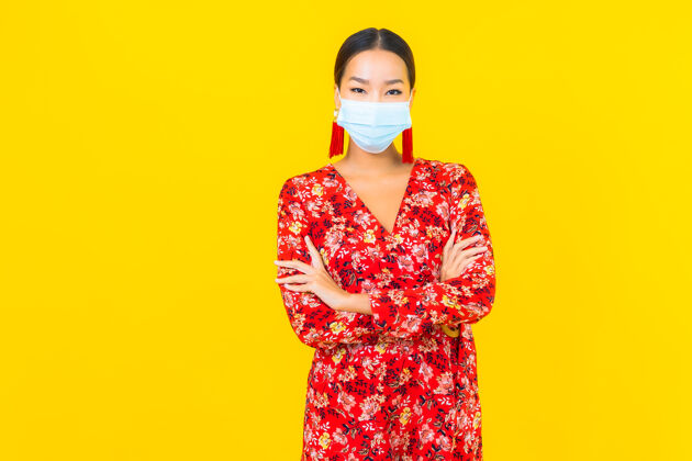 人肖像美丽的亚洲年轻女子戴上防冠状病毒或冠状病毒的面具在黄色的墙上冠状病毒亚洲人预防
