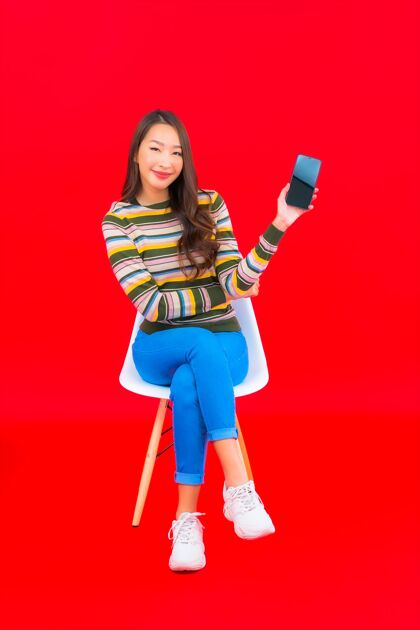 女在红色的隔离墙上画一幅美丽的亚洲年轻女子手持智能手机的画像杯子看年轻