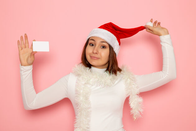 肖像正面图年轻女性手持白色银行卡在粉色墙上圣诞假期新年时尚彩钱圣诞节年轻的女性风景