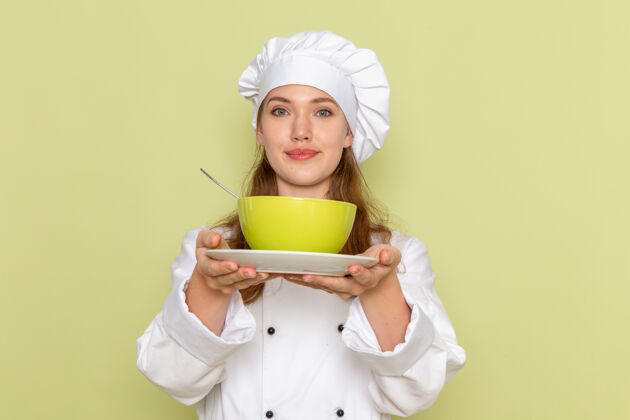 盘子身穿白色厨师服的女厨师手持绿色盘子 微笑着站在绿色墙壁上的正视图帽子国内烹饪