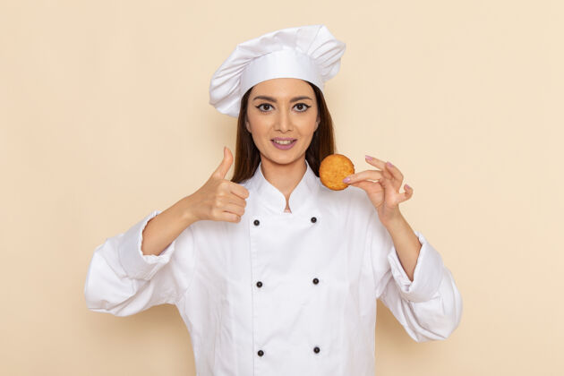 成人身穿白色厨师服的年轻女厨师正拿着小饼干站在浅白的墙上厨房前面人