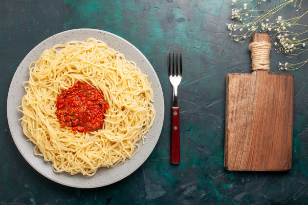 盘子俯视图：深蓝色表面上有肉末和番茄酱的熟意大利面食意大利面面团意大利面