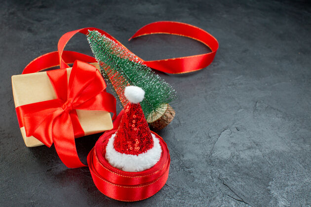 甜点俯瞰圣诞老人帽子上的一卷丝带和美丽的礼物圣诞树在黑暗的背景景观鲜花圣诞节