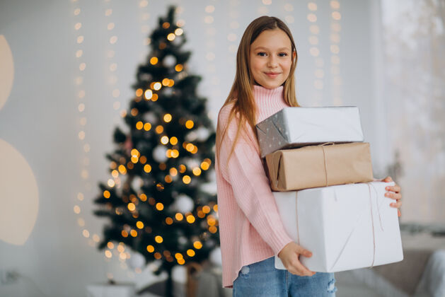可爱的可爱的女孩拿着圣诞礼物在圣诞树旁礼物微笑乐趣