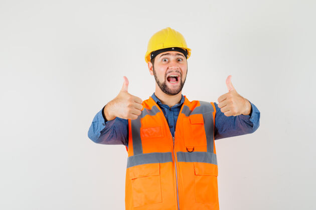 安全帽年轻的建设者在衬衫 背心 头盔上竖起大拇指 看上去很幸运 正视图工人工程师工业