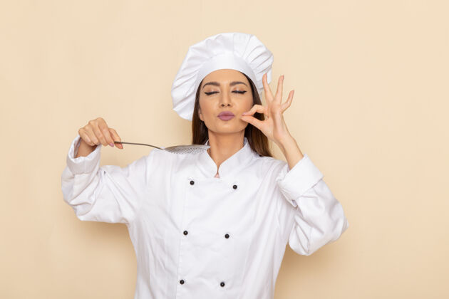 正面身穿白色厨师服的年轻女厨师正拿着大银勺站在白色的墙上女性人烹饪