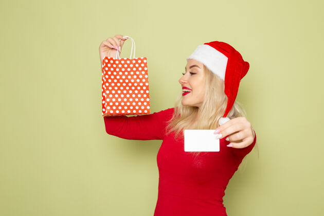 小正面风景美丽的女人拿着礼物在小包装和银行卡在绿色的墙上情感节日圣诞雪彩新年银行漂亮雪