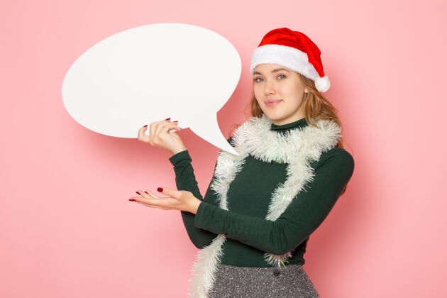 年轻的女性正面图年轻女性手持粉色墙上的白色大招牌圣诞新年造型节日色彩感慨大圣诞节帽子