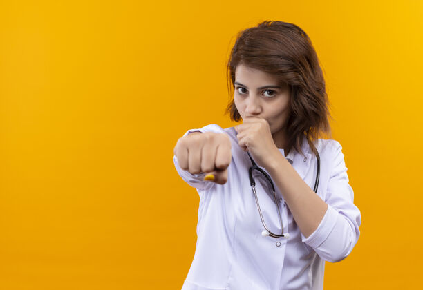 指着穿着白大褂的年轻女医生用听诊器叮当作响的拳头指着相机医生听诊器拳头