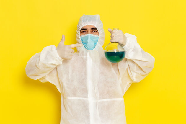 实验室黄色办公桌上穿着特殊防护服戴口罩的男性科学工作者正面图科学工作者服装颜色危险照片手持男性外套