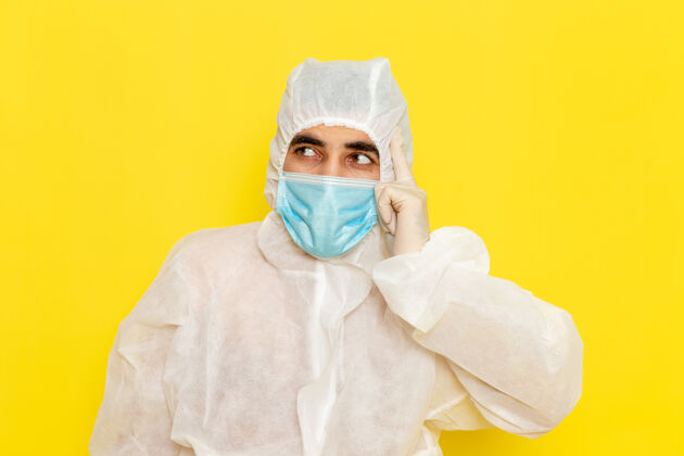正面身穿白色特殊防护服 带无菌口罩的男性科学工作者的正面图黄色墙壁上的思考特殊思维防护