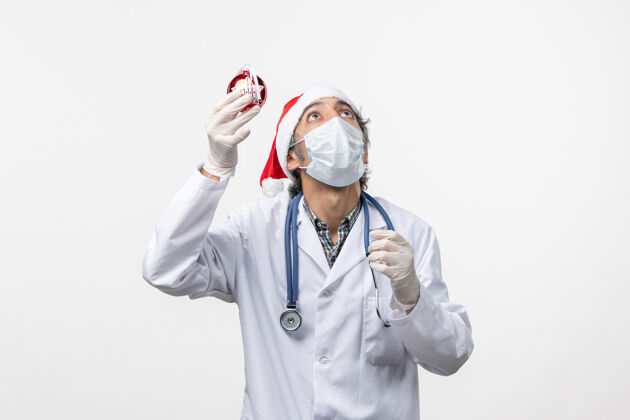 外套正面图戴面具的男医生带着玩具在白墙上健康的柯维德假日病毒冠状病毒圣诞节实验室外套