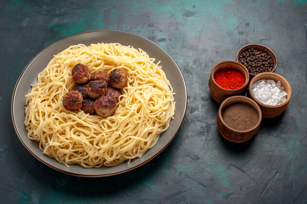 调味品半俯视图煮熟的意大利面食 深蓝色表面有肉丸和调味品生的食物晚餐