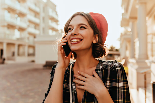 漂亮戴着贝雷帽的幸福美丽的女孩在打电话漂亮的短发女人拿着智能手机走在街上成人红色情绪