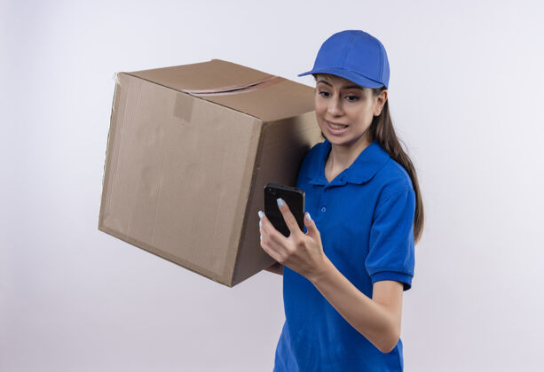 帽子身穿蓝色制服 头戴鸭舌帽的年轻送货女拿着大纸箱看着手机屏幕忧心忡忡屏幕制服电话