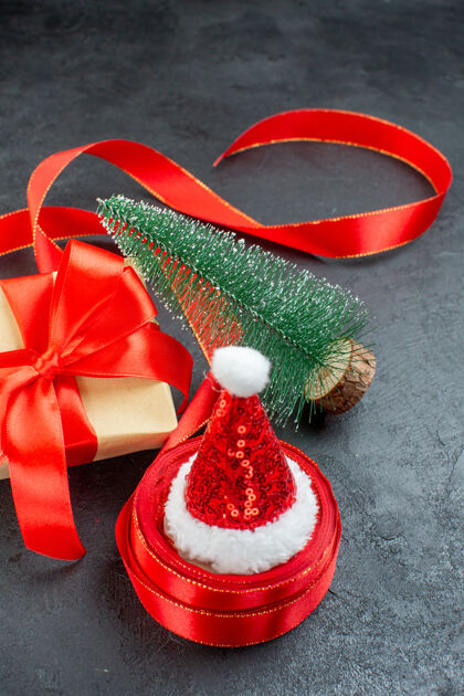 鞠躬一卷彩带上的圣诞老人帽子和黑色背景上的圣诞树的美丽礼物的垂直视图圣诞老人的帽子查看滚动