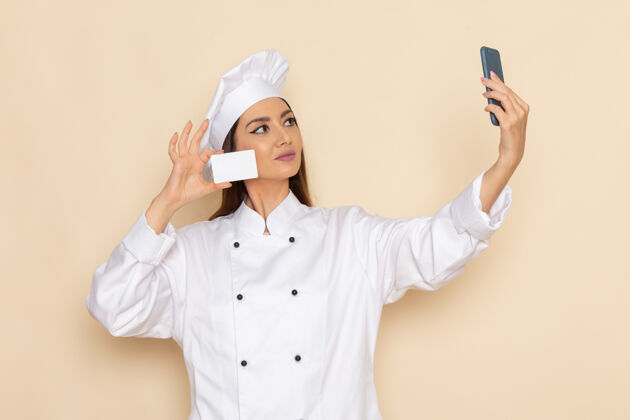 前面身穿白色厨师服的年轻女厨师手持卡片 在浅白的墙上自拍厨房女性举行