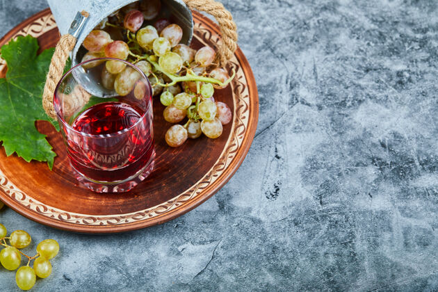 盘子一桶葡萄和一杯果汁放在大理石上水果串玻璃