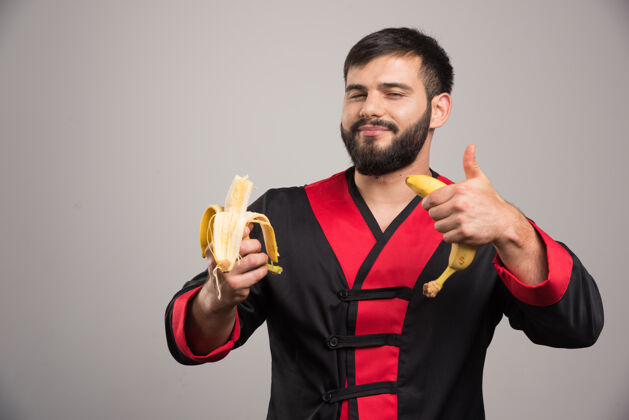 人男人伸出大拇指 在灰色的地面上吃香蕉食物模型人