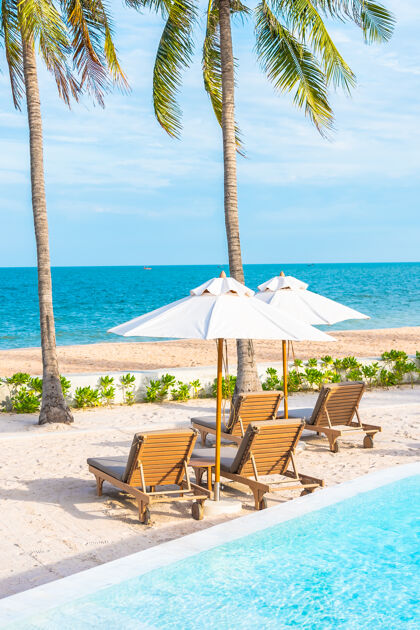甲板酒店度假区的户外游泳池周围有雨伞和躺椅 有海边沙滩和椰子树游客豪华酒店