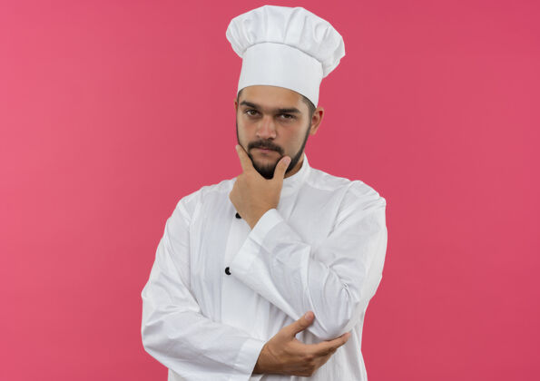 空间体贴的年轻男厨师身着厨师制服 手放在下巴和手肘上 与粉色空间隔离体贴下巴粉色