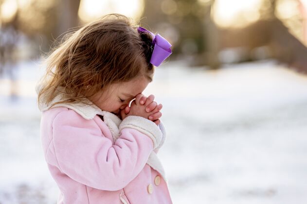 女性小女孩在阳光下的雪地花园里祈祷 距离模糊圣经孩子信仰