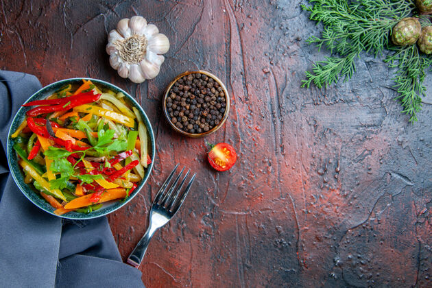 地方顶视图蔬菜沙拉在碗里群青蓝色披肩大蒜黑胡椒叉在暗红色的桌子上复制的地方饭大蒜蔬菜沙拉