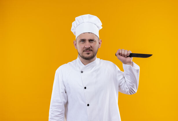 帅气年轻帅气的厨师穿着厨师制服拿着刀孤立在橙色的空间刀厨师橙色