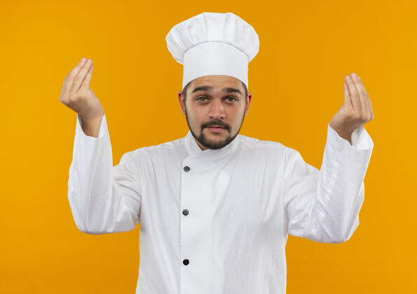 手势身着厨师制服的年轻男厨师在橙色空间做着看起来孤立的小费手势橙色烹饪男性