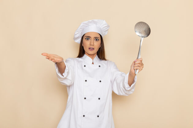 年轻身穿白色厨师服的年轻女厨师正拿着大银勺站在白墙上西装女工作