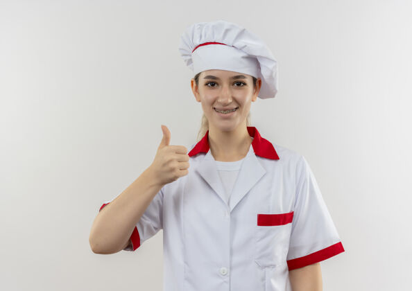 看微笑着的年轻漂亮厨师身着厨师制服 戴着牙套 大拇指朝上 在空白处显得孤立年轻厨师厨师