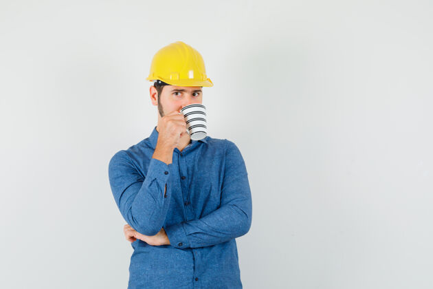 计划年轻工人一边喝咖啡一边穿着衬衫 头盔思考办公室工程师工作