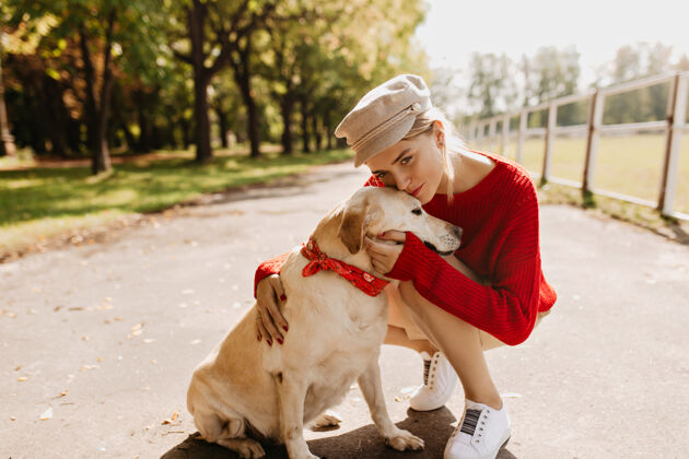 玩耍穿着时髦衣服的漂亮年轻女子温柔地亲吻着她的狗美丽的金发女郎和她的宠物在公园里享受阳光明媚的天气散步哺乳动物拉布拉多