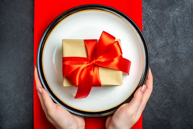 空盘子上图为国家圣诞大餐背景 黑色桌子上的红色餐巾上 手拿着空盘子 上面系着蝴蝶结形状的红丝带用餐鞠躬圣诞节