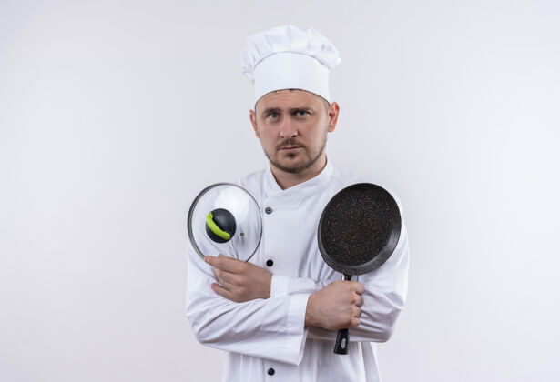看年轻帅气的厨师穿着厨师制服 手里拿着煎锅和锅盖 在白色的空间里显得与世隔绝烹饪复制持有