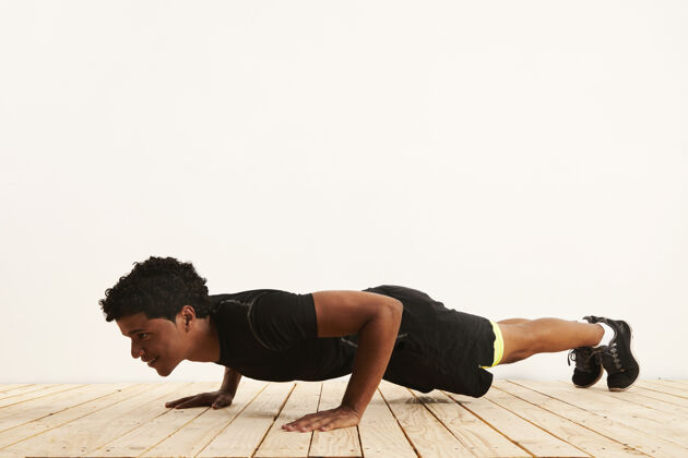健身房年轻的黑人运动员微笑着在白色的墙壁上做俯卧撑身体年轻肌肉