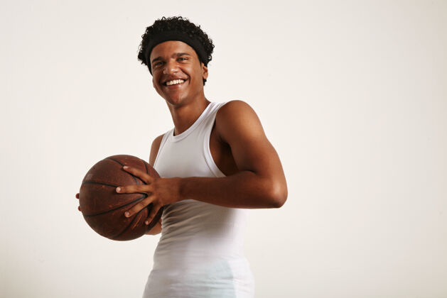 职业年轻的非洲裔美国人 穿着一件白色无袖衬衫 头上戴着一条带 胸前挂着一个脏兮兮的皮革篮球 与白色隔离开来球严肃游戏