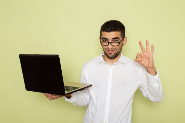 工作身穿白衬衫的男办公室工作人员手持和使用笔记本电脑在绿色墙上的正面视图衬衫持有人