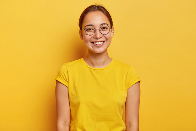 眼镜水平快照的亚洲女大学生戴着大圆圆的眼镜 黄色的休闲装 轻轻的微笑 满意的一天大学毕业后 穿上了夏天的黄色T恤眼镜明亮微笑