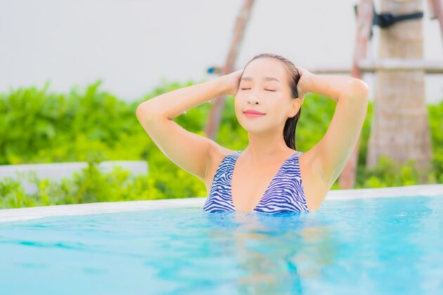 游泳池肖像美丽的亚洲年轻女子放松休闲周围的室外游泳池与海洋海滩花景观酒店