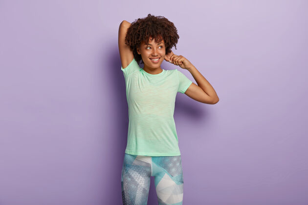 运动满意的深色皮肤女人的照片伸展双手 在健身训练前热身 穿着运动服 有很好的灵活性 专注在一边 隔离在紫色的墙壁上锻炼概念站立室内发型