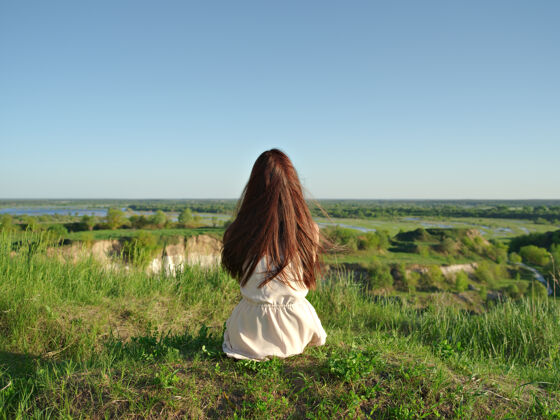女孩放松的年轻女子看着窗外的景色安静的女孩坐在悬崖边欣赏风景-户外草地夏天自由