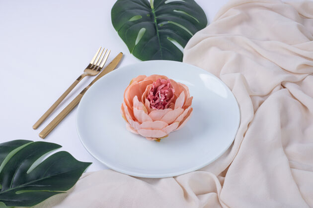 常绿一朵玫瑰放在白色的盘子里 上面有假叶子和桌布装饰假的餐具